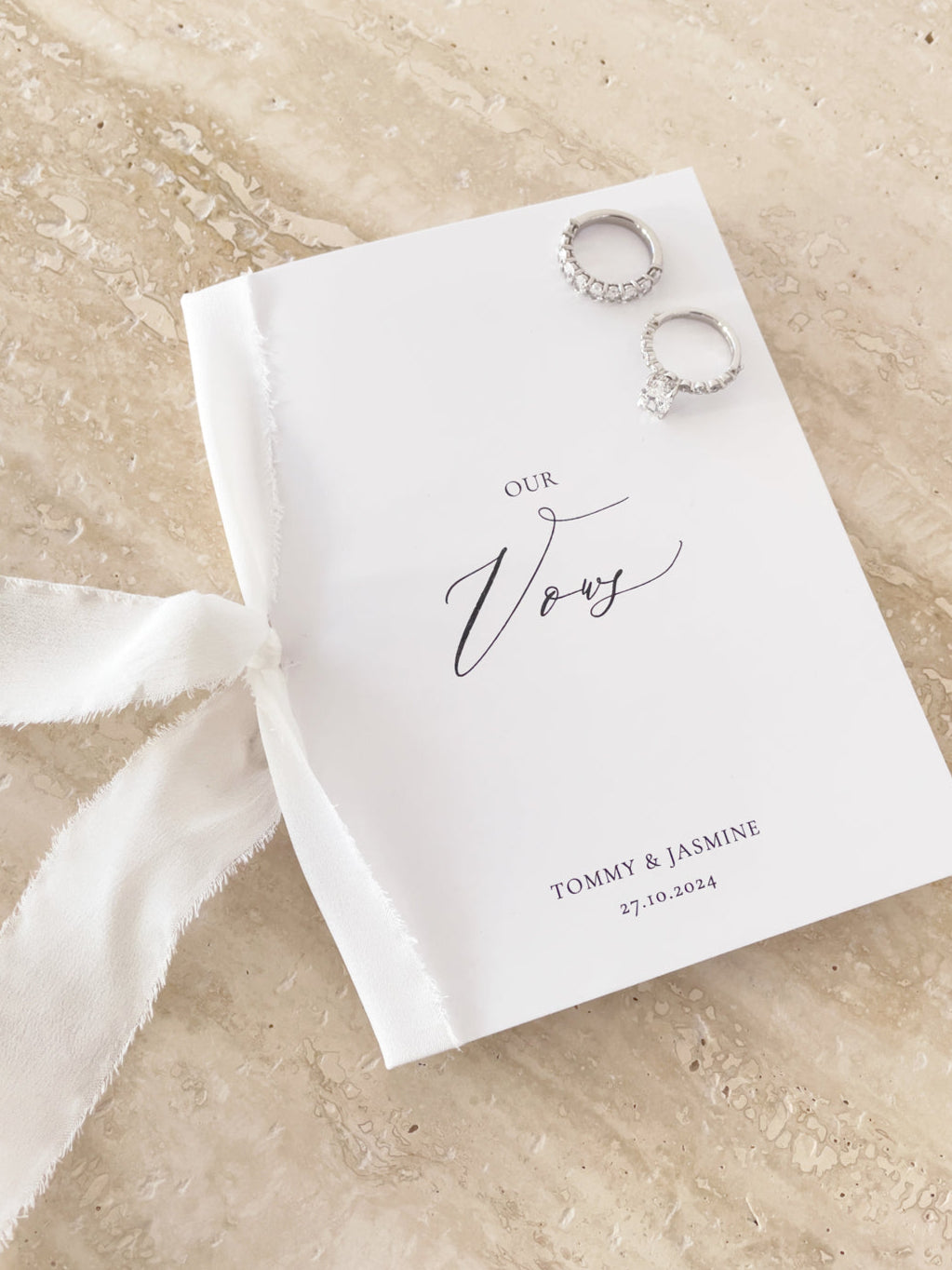 A personalised white wedding vow book with a silk ribbon, featuring the names of the couple and the wedding date on the cover, tied with a white silk ribbon.