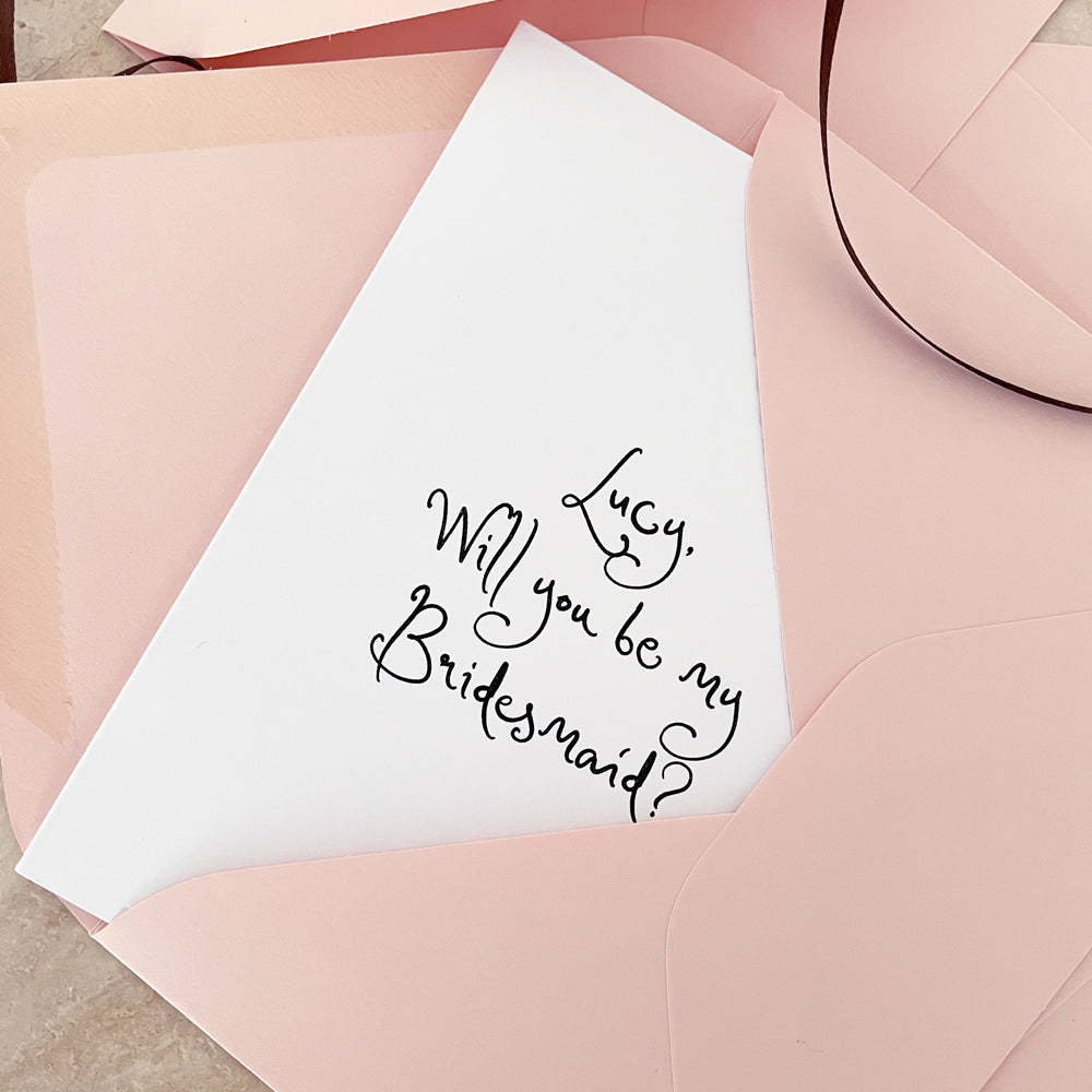 
                      
                        White card with 'Will you be my Bridesmaid?' text on a pink envelope.
                      
                    